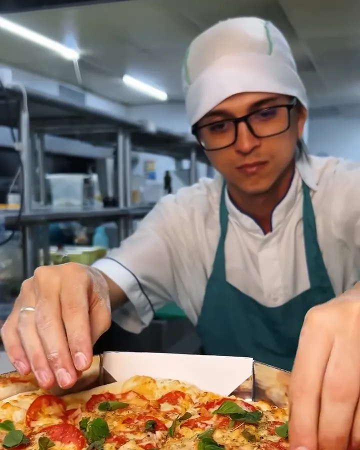 Pizzaiola finalizando a pizza com manjericão