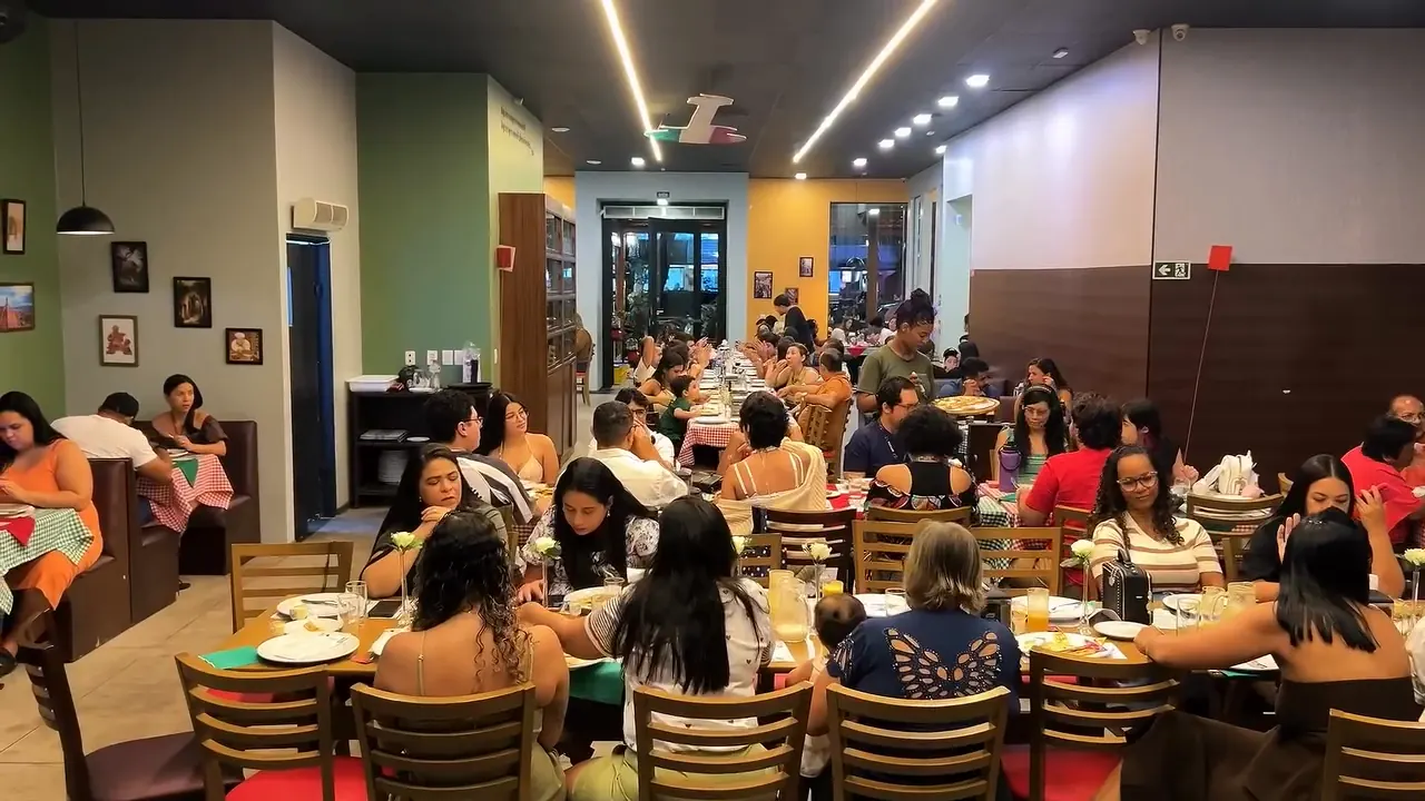 Salão da La Parmigiana cheio de famílias, com mesas de toalha xadrez e luminárias pendentes